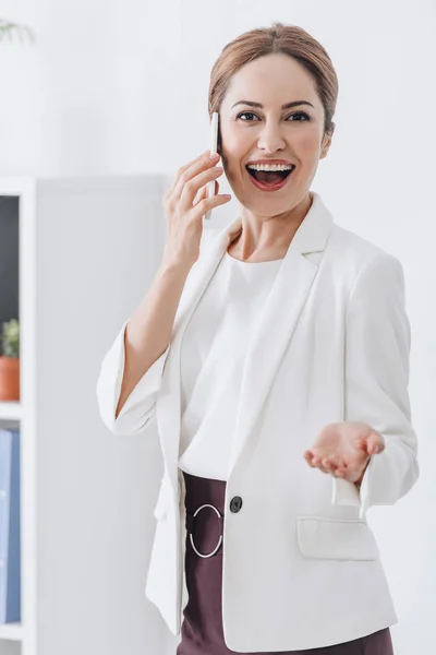 Hermosa mujer de negocios alegre hablando en el teléfono inteligente en la oficina - foto de stock