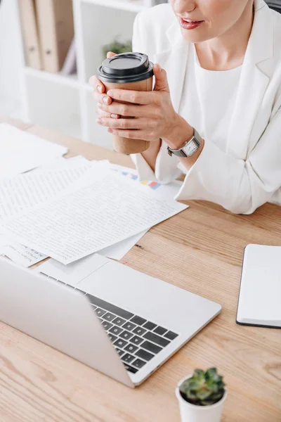 Ausgeschnittene Ansicht einer Geschäftsfrau mit Coffee to go am Arbeitsplatz mit Dokumenten und Laptop — Stockfoto
