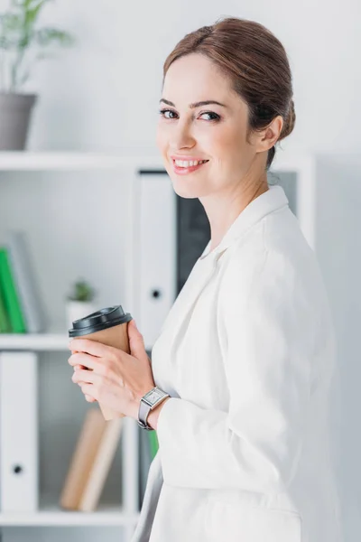 Mulher de negócios alegre atraente com café para ir no escritório moderno — Fotografia de Stock