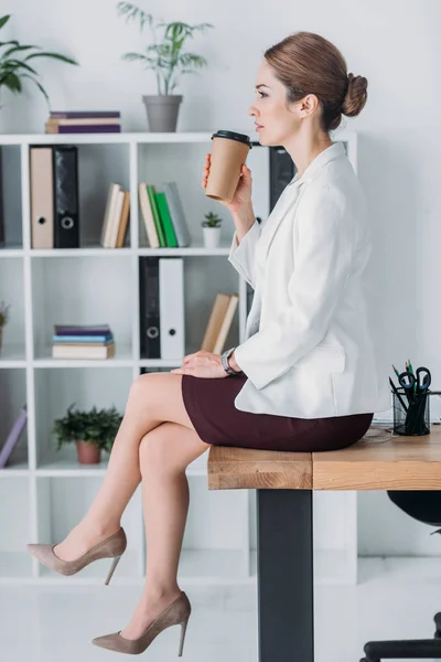 Geschäftsfrau mit Pappbecher sitzt während der Kaffeepause im Büro auf dem Tisch — Stockfoto