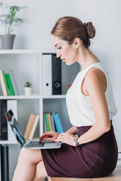 Serious businesswoman working with laptop while sitting on table in office — Stock Photo