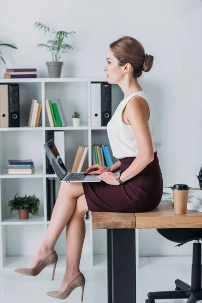 Executive serious business woman using laptop while sitting on table in office — Stock Photo