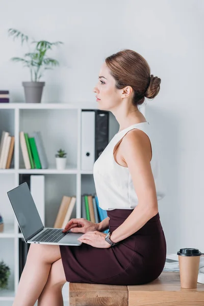 Business woman working with laptop while sitting on table with coffee to go in office — Stock Photo