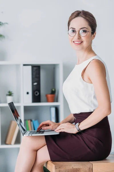 Confident businesswoman working with laptop while sitting on table in office — Stock Photo
