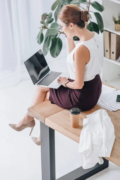 Femme d'affaires travaillant avec un ordinateur portable tout en étant assis sur la table dans le bureau — Photo de stock