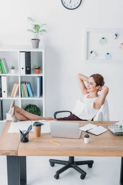 Entspannt fröhliche Geschäftsfrau sitzt im Stuhl mit der Hand hinter dem Kopf am Arbeitsplatz — Stockfoto