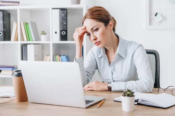 Exhausted adult businesswoman with headache touching her head while sitting at office — Stock Photo