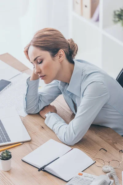 Blick aus der Vogelperspektive auf eine überarbeitete erwachsene Geschäftsfrau, die am Arbeitsplatz in einem modernen Büro schläft — Stockfoto