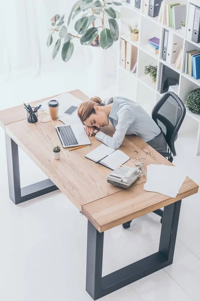 Высокий угол зрения перегруженной работой взрослой бизнесвумен спит на рабочем месте — стоковое фото