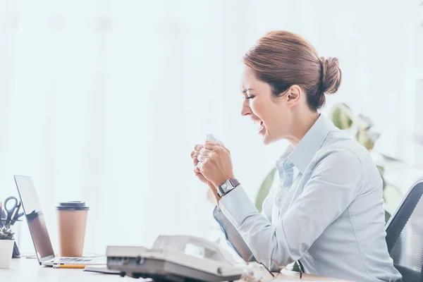 Вид збоку божевільної дорослої бізнес-леді розсипаючи папір на робочому місці — стокове фото