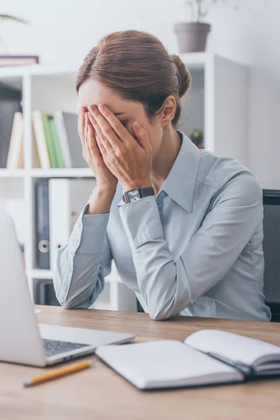 Stressed adult businesswoman covering face with hands at workplace — Stock Photo