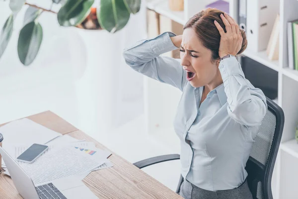 Vue grand angle de la femme d'affaires stressée tenant sa tête et criant sur le lieu de travail — Photo de stock