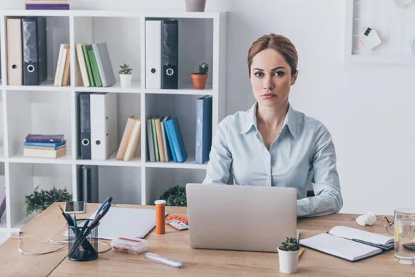 Serious adult businesswoman with medicines on workplace looking at camera — Stock Photo