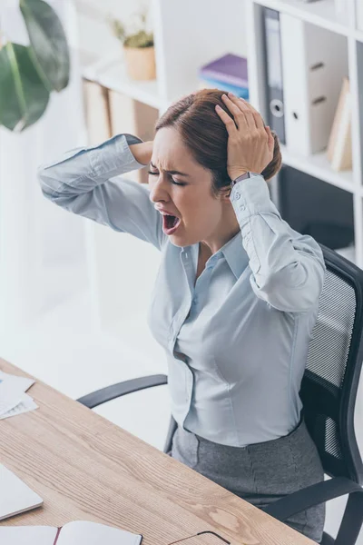 Високий кут зору стресованої дорослої бізнес-леді тримає голову і кричить на робочому місці — стокове фото