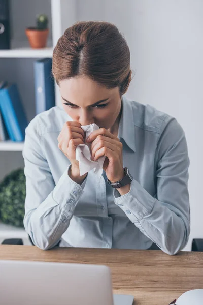 Mujer de negocios adulta enferma con nariz líquida sosteniendo servilleta de papel y sentada en el lugar de trabajo — Stock Photo