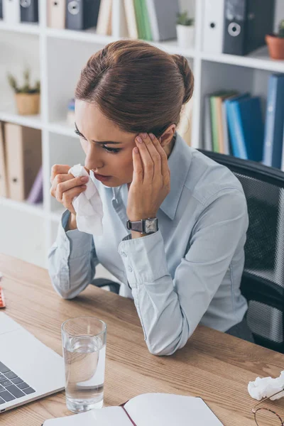 Vue grand angle de femme d'affaires adulte malade avec serviette en papier et verre d'eau assis sur le lieu de travail — Photo de stock