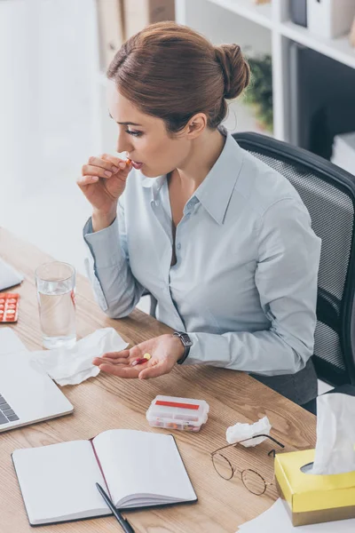 Blick aus der Vogelperspektive auf kranke erwachsene Geschäftsfrau, die Pillen am Arbeitsplatz nimmt — Stockfoto