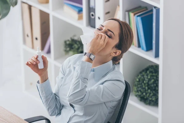 Vue grand angle de malade adulte femme d'affaires pulvérisation son nez au bureau — Photo de stock