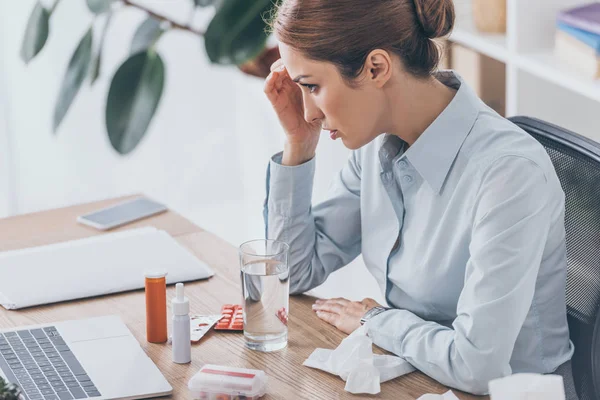 Traurig kranke Geschäftsfrau sitzt mit verschiedenen Medikamenten am Arbeitsplatz — Stockfoto