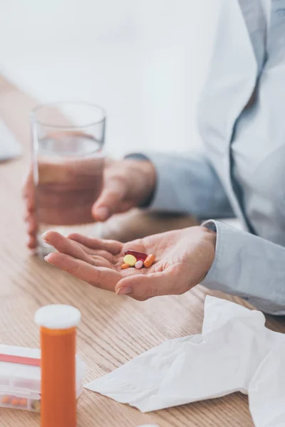 Tiro cortado de empresária doente sentado no local de trabalho com pílulas e copo de água — Fotografia de Stock
