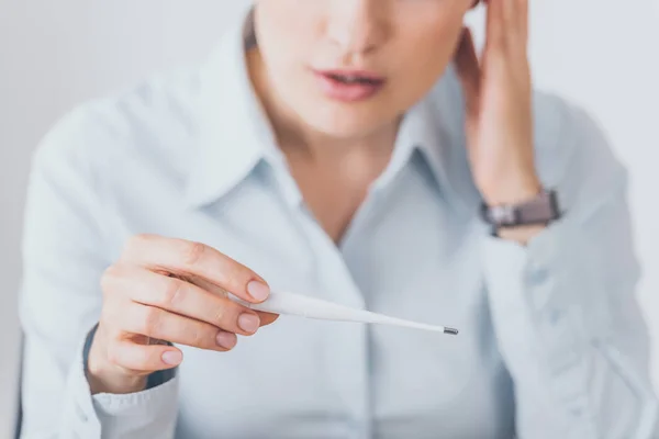 Recortado tiro de enferma mujer de negocios sentado en el lugar de trabajo y la celebración de termómetro eléctrico - foto de stock