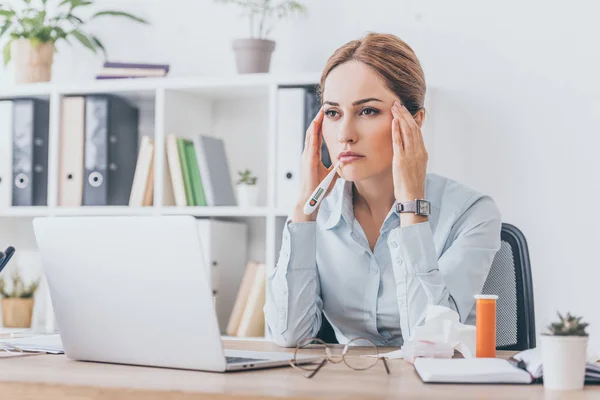 Erwachsene kranke Geschäftsfrau mit Kopfschmerzen sitzt am Arbeitsplatz und schaut weg — Stockfoto