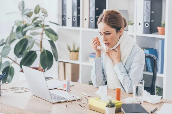 Femme d'affaires adulte malade avec écharpe assis sur le lieu de travail dans un bureau moderne — Photo de stock