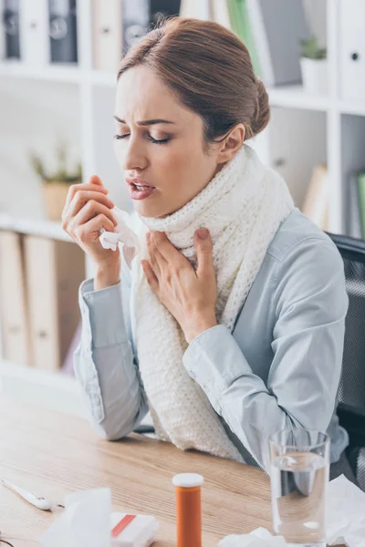 Adult sick businesswoman with cough sitting at workplace in scarf — Stock Photo