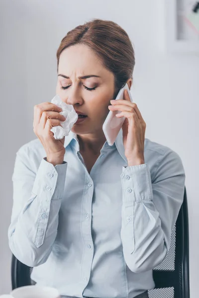 Retrato de cerca de la mujer de negocios adulta con secreción nasal hablando por teléfono en la oficina - foto de stock