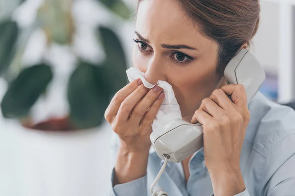 Close-up portrait of businesswoman with runny nose talking by wired phone — Stock Photo