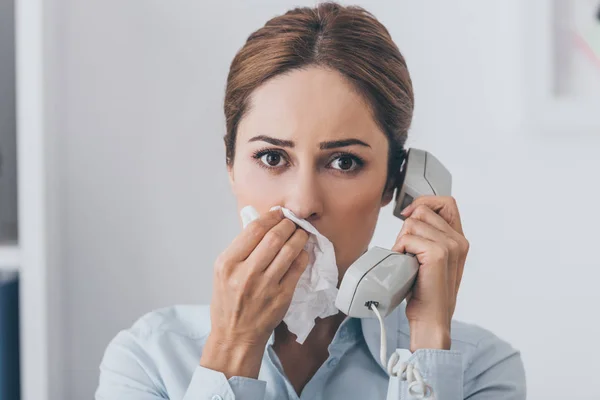 Portrait en gros plan d'une femme d'affaires avec le nez qui coule parlant par téléphone filaire et regardant la caméra — Photo de stock