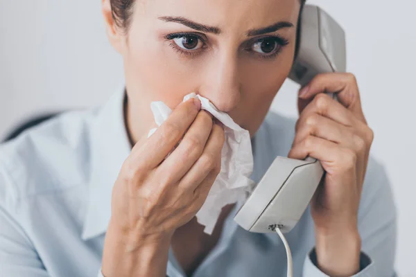 Close-up portrait of sad businesswoman talking by wired phone with paper napkin at office — Stock Photo