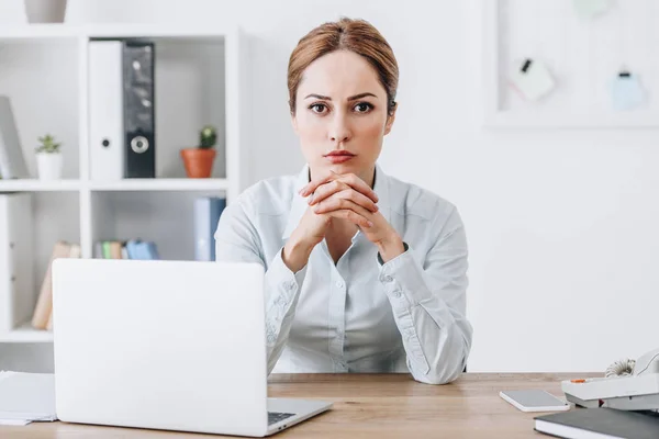 Serious businesswoman sitting at workplace and looking at camera at office — Stock Photo