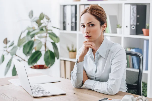 Ernsthafte erwachsene Geschäftsfrau sitzt am Arbeitsplatz im Büro und schaut in die Kamera — Stockfoto
