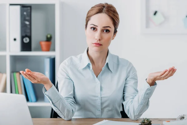 Serious adult businesswoman looking at camera and gesturing with hands at office — Stock Photo