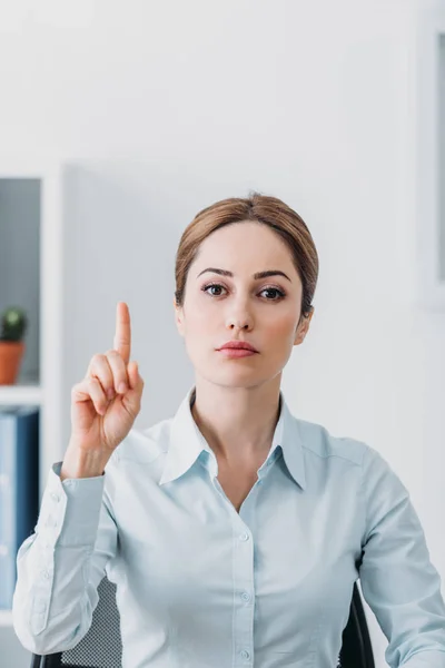 Serious adult businesswoman looking at camera and pointing up at office — Stock Photo
