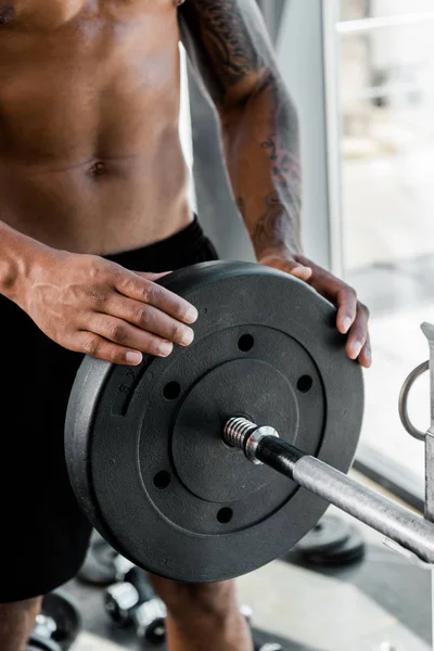 Primer plano vista parcial de muscular joven deportista poniendo placa de peso en la barra en el gimnasio - foto de stock