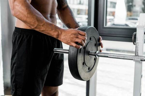 Recortado disparo de muscular joven deportista poner placa de peso en la barra en el gimnasio - foto de stock