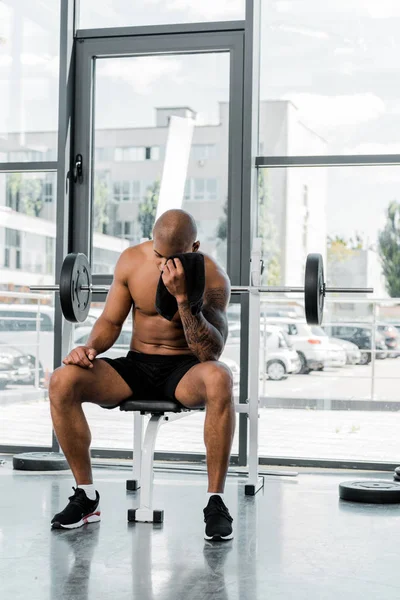 Joven deportista muscular limpiando la frente con toalla mientras está sentado después del entrenamiento en el gimnasio — Stock Photo