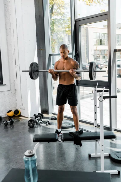 Vista completa de musculoso sin camisa afroamericano hombre levantando la barra en el gimnasio - foto de stock