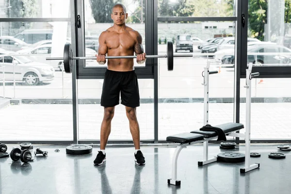 Muskulöser junger Sportler mit Langhantel und Blick in die Kamera im Fitnessstudio — Stockfoto