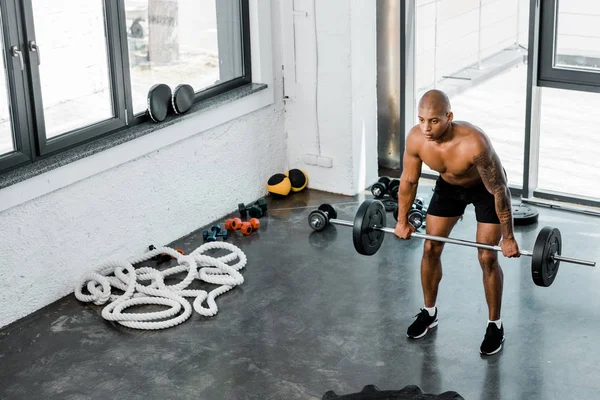 Vista de ángulo alto del joven deportista musculoso sin camisa levantando la barra en el gimnasio - foto de stock