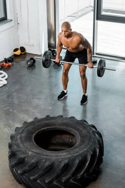 Vista de ángulo alto de atlético desnudo pecho africano americano deportista levantando la barra en el gimnasio - foto de stock