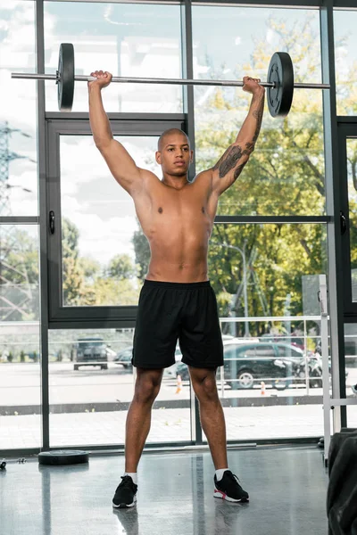 Американский спортсмен с голыми грудями поднимает штангу в спортзале — стоковое фото