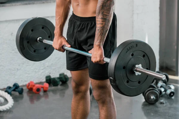 Recortado disparo de muscular joven deportista celebración de la barra en el gimnasio - foto de stock