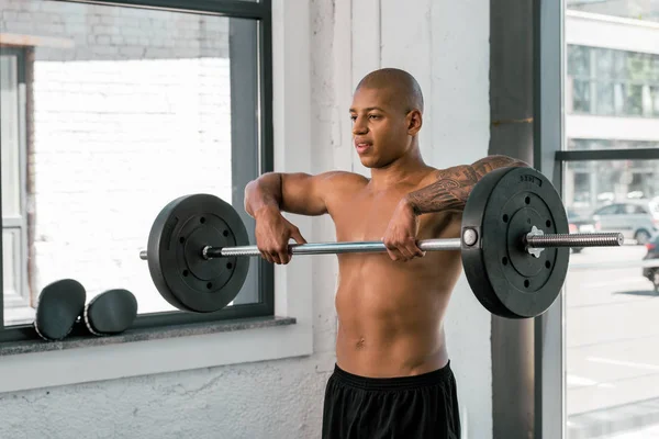 Handsome young african american sportsman lifting barbell in gym — Stock Photo