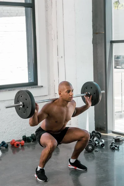 Joven atlético afroamericano hombre levantando la barra y mirando hacia otro lado en el gimnasio - foto de stock