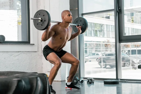 Musculoso joven afroamericano deportista levantando la barra en el gimnasio - foto de stock