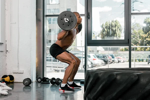 Вид сбоку на мускулистого спортсмена, поднимающего штангу и смотрящего в спортзале — стоковое фото