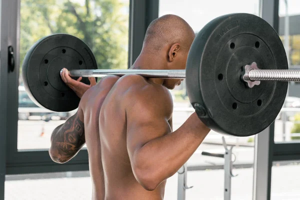 Back view of muscular young sportsman lifting barbell in gym — Stock Photo